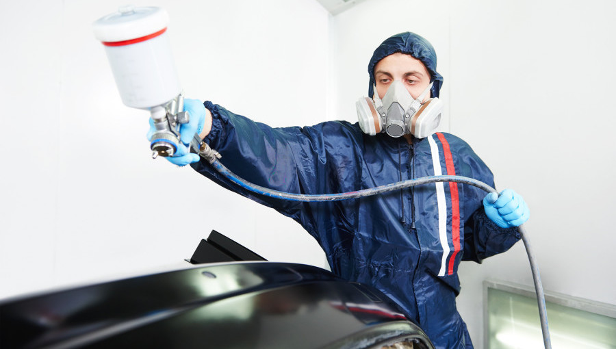 worker  painting auto car bumper in a paint chamber during repair work